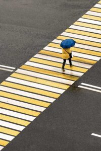 Woman walking across the street with an umbrella on her way to her depression therapist port jefferson